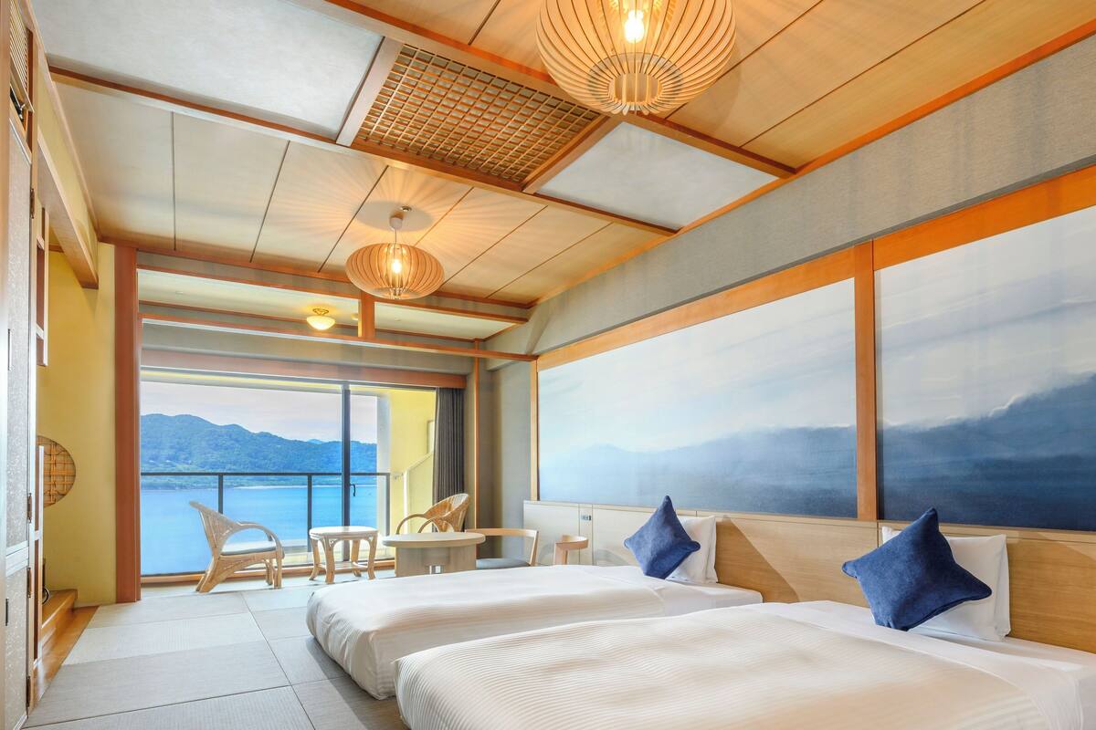 Ein Hotelzimmer mit zwei Betten, einem kleinen Tisch, Stühlen und Meerblick.