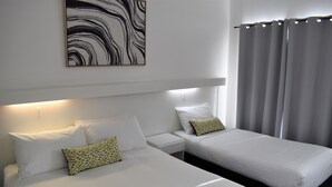 Una habitación de hotel con dos camas, ropa de cama blanca, una mesita de noche, una obra de arte colgada en la pared y una cortina.
