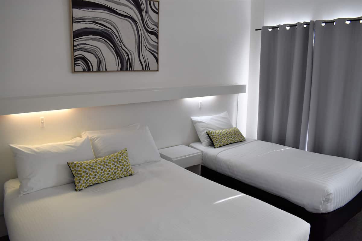 A hotel room with two beds, white bedding, a nightstand, a wall-mounted artwork, and a curtain.