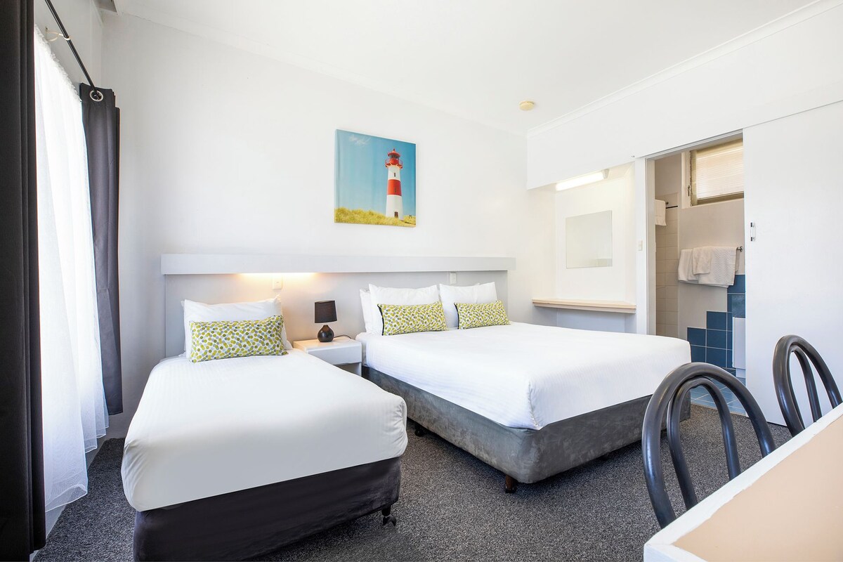 Een hotelkamer met twee bedden, een schilderij van een vuurtoren, een bureau en een stoel.