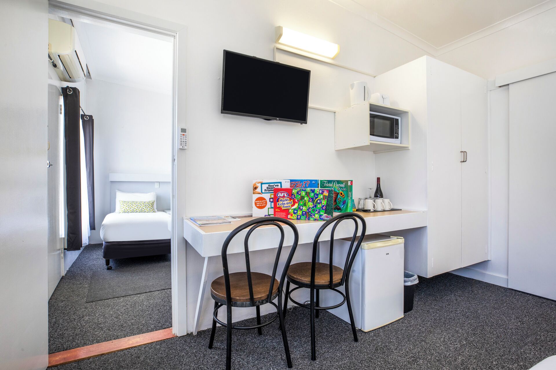 Une chambre d’hôtel compacte comprenant un lit, un bureau avec deux chaises, un téléviseur à écran plat, un four à micro-ondes et une petite kitchenette.