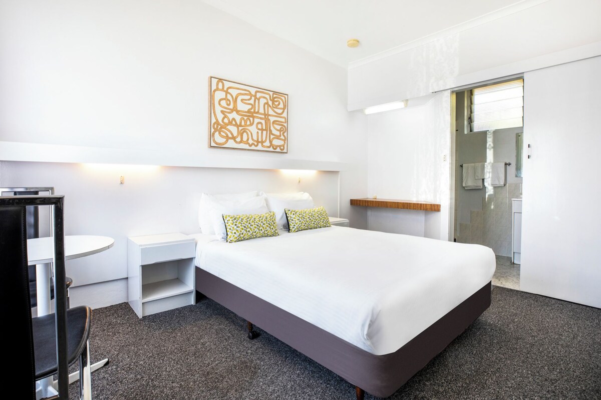 Een hotelkamer met een groot bed, een nachtkastje, een stoel en een klein rond tafeltje.