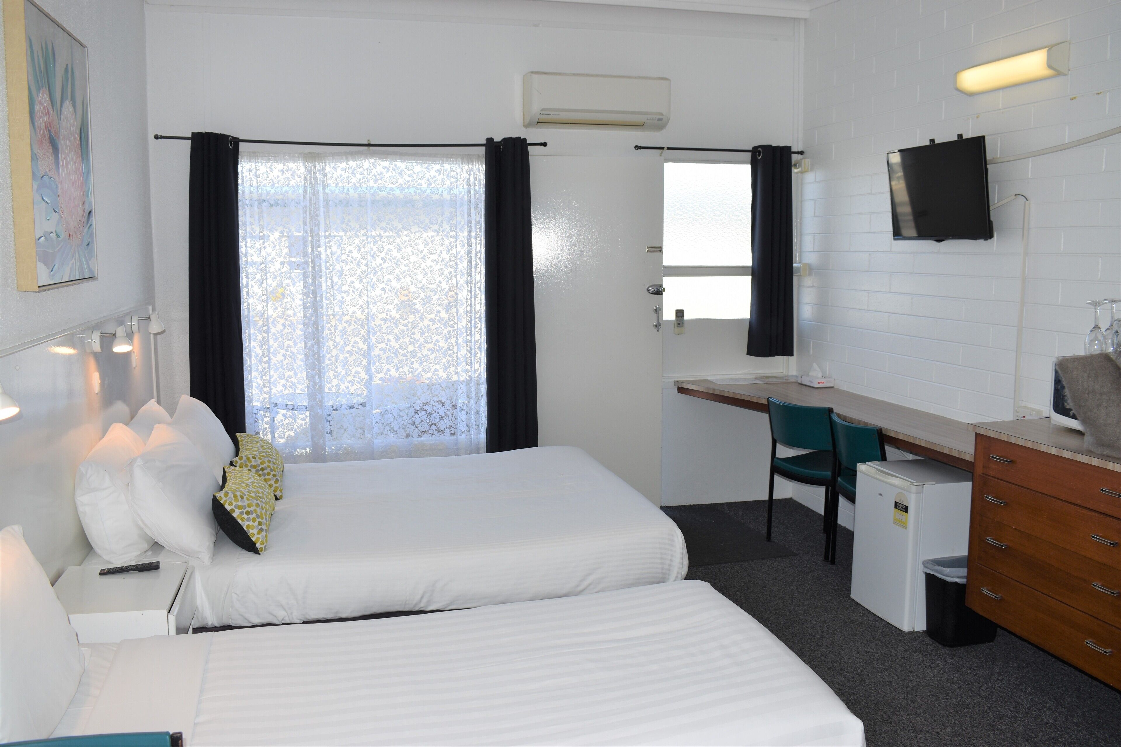 Habitación de hotel con dos camas, un escritorio, una silla, un televisor y un refrigerador pequeño.