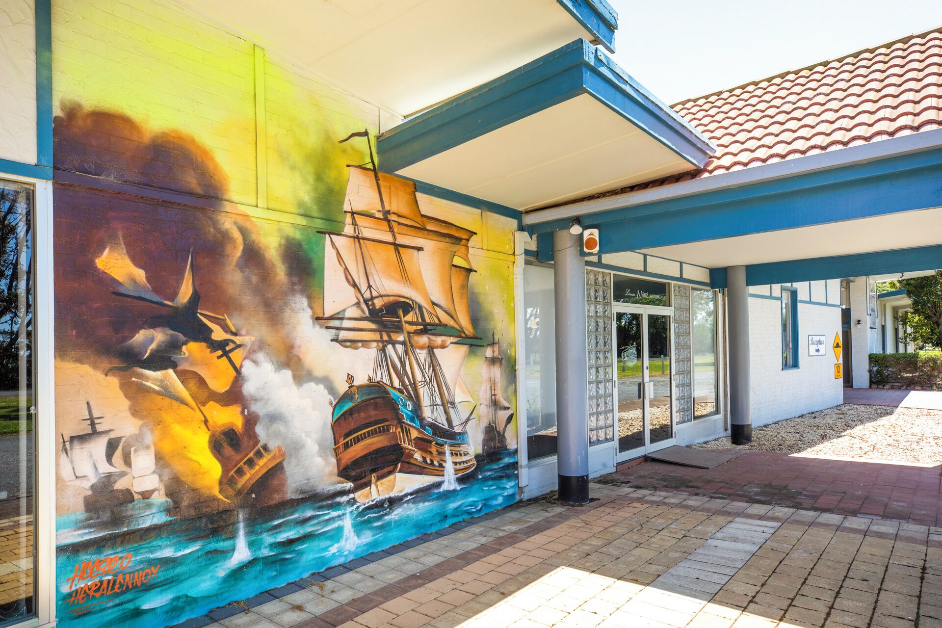 A building with a mural of a ship and ocean, a covered walkway, and a reception area.