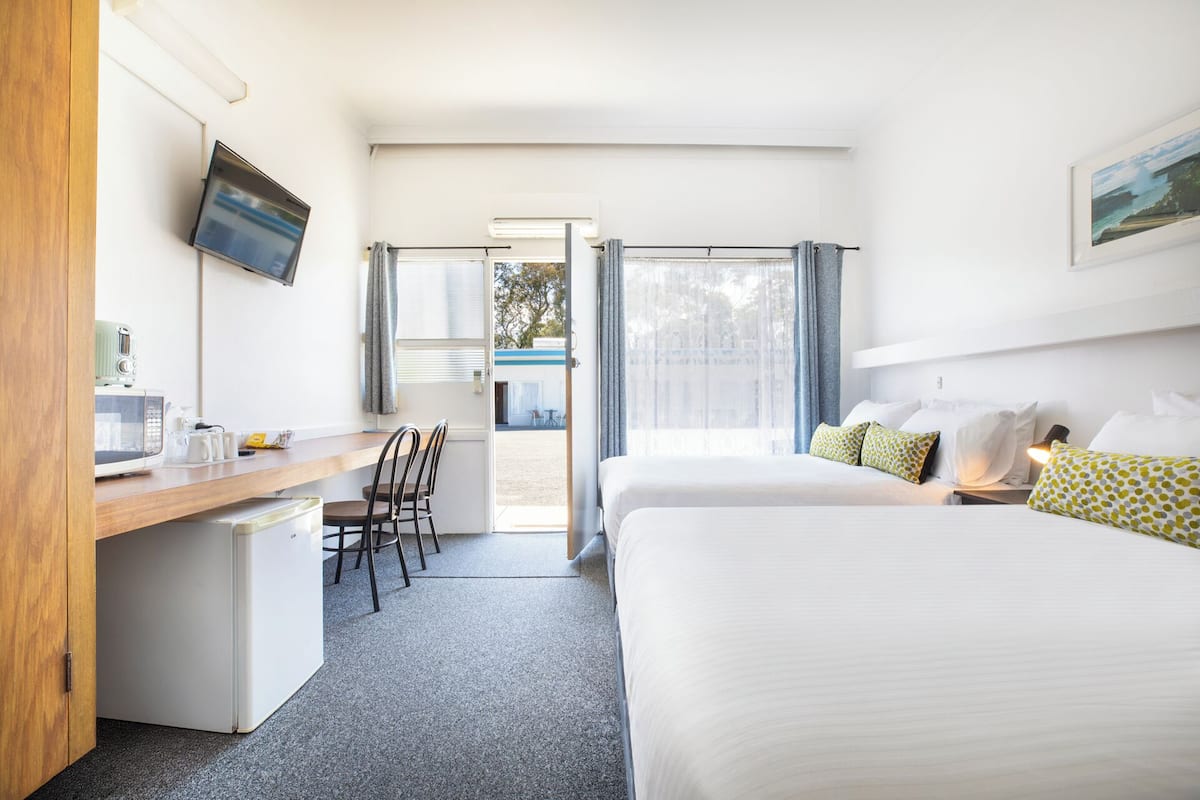 A hotel room with a bed, a desk, a chair, a TV, and a window.
