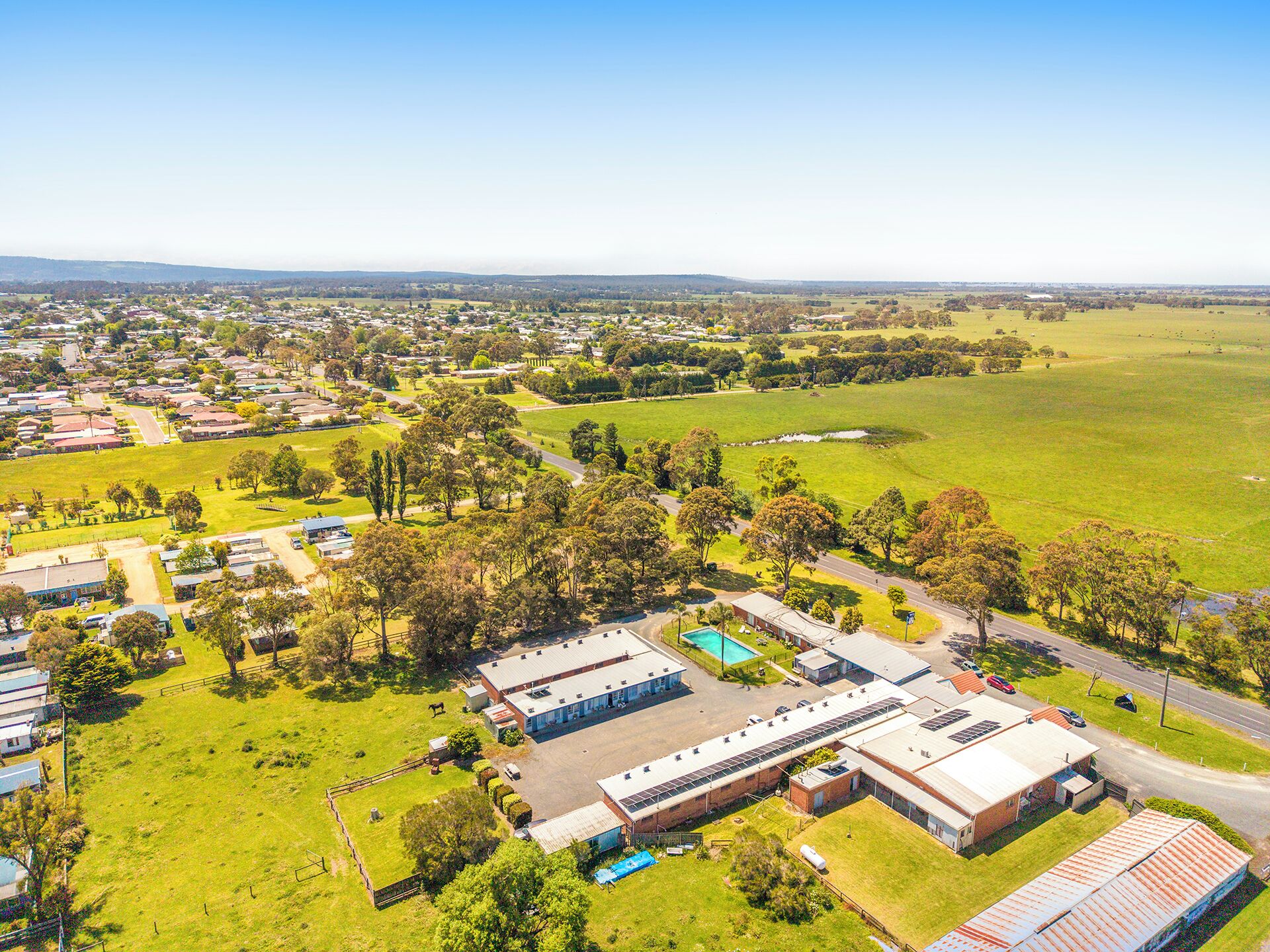 Vista aérea de una zona residencial con casas, un extenso campo abierto y un edificio comercial con piscina.
