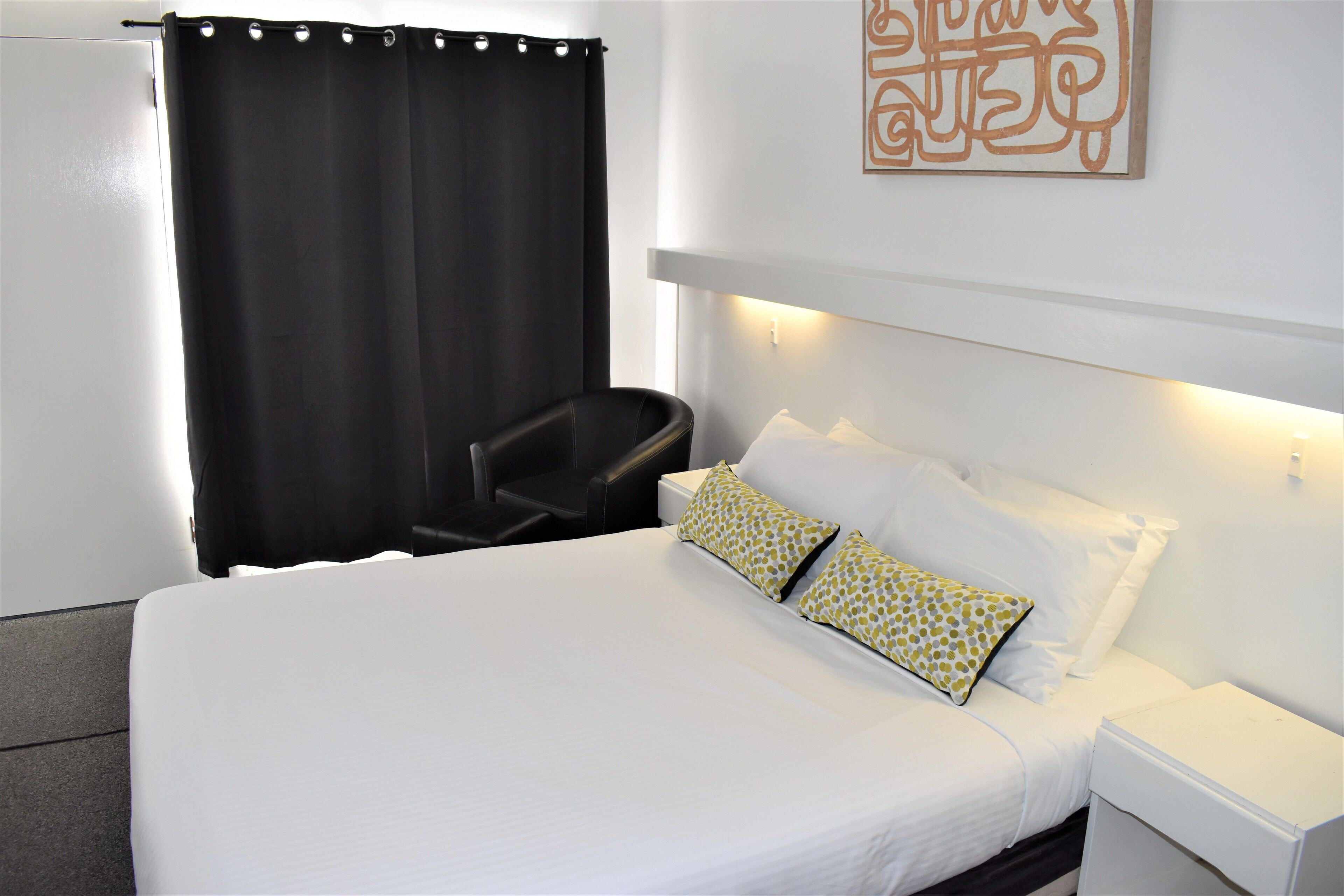 A hotel room with a bed, a chair, a nightstand, and a wall-mounted light fixture.