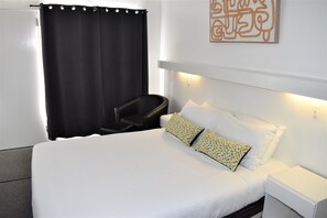 A hotel room with a bed, a chair, a nightstand, and a wall-mounted light fixture. - Ship Motel Yarram (Yarram)