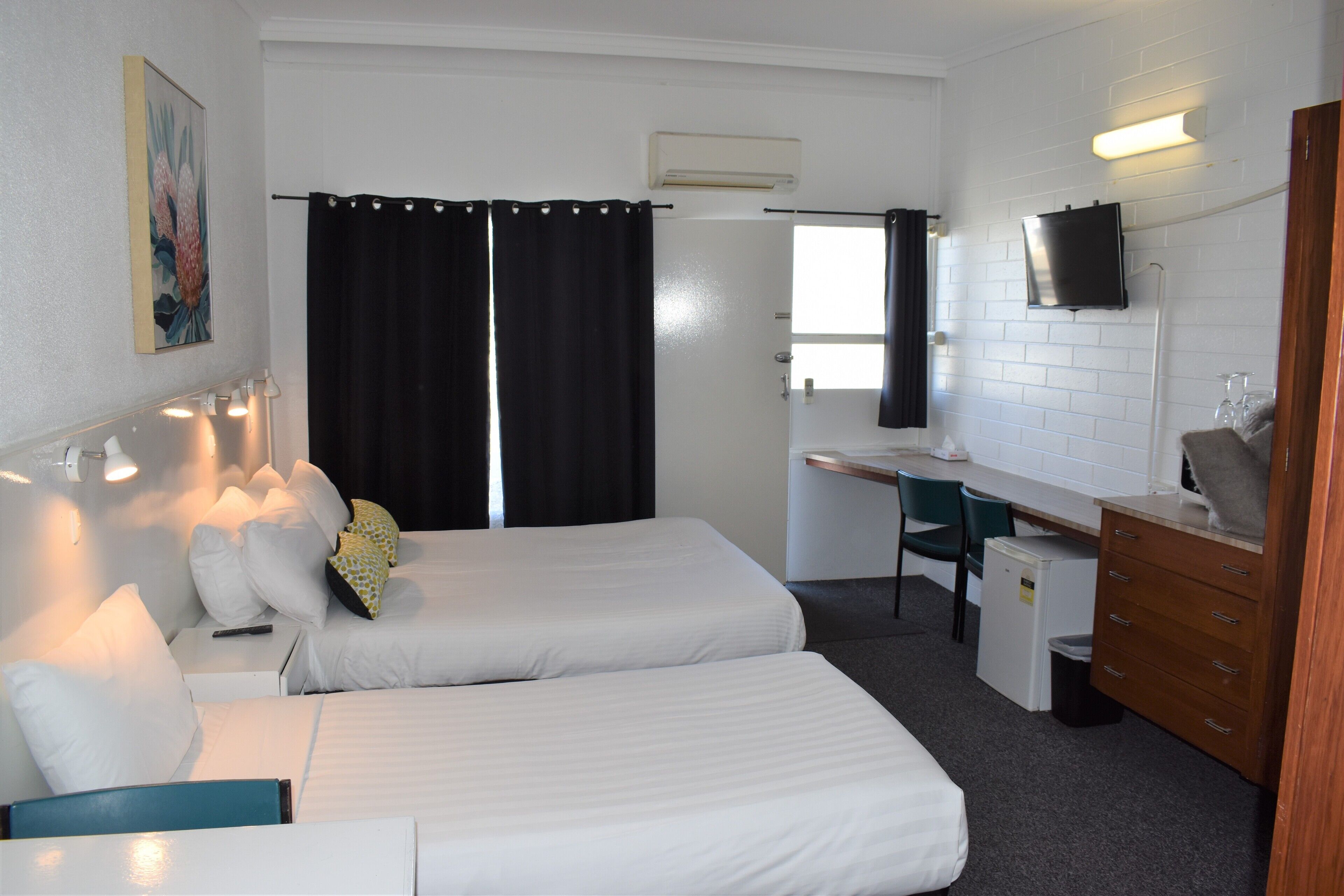 A hotel room with two beds, a desk, a chair, a TV, and a small refrigerator.