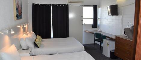 A hotel room with two beds, a desk, a chair, a TV, and a small refrigerator.