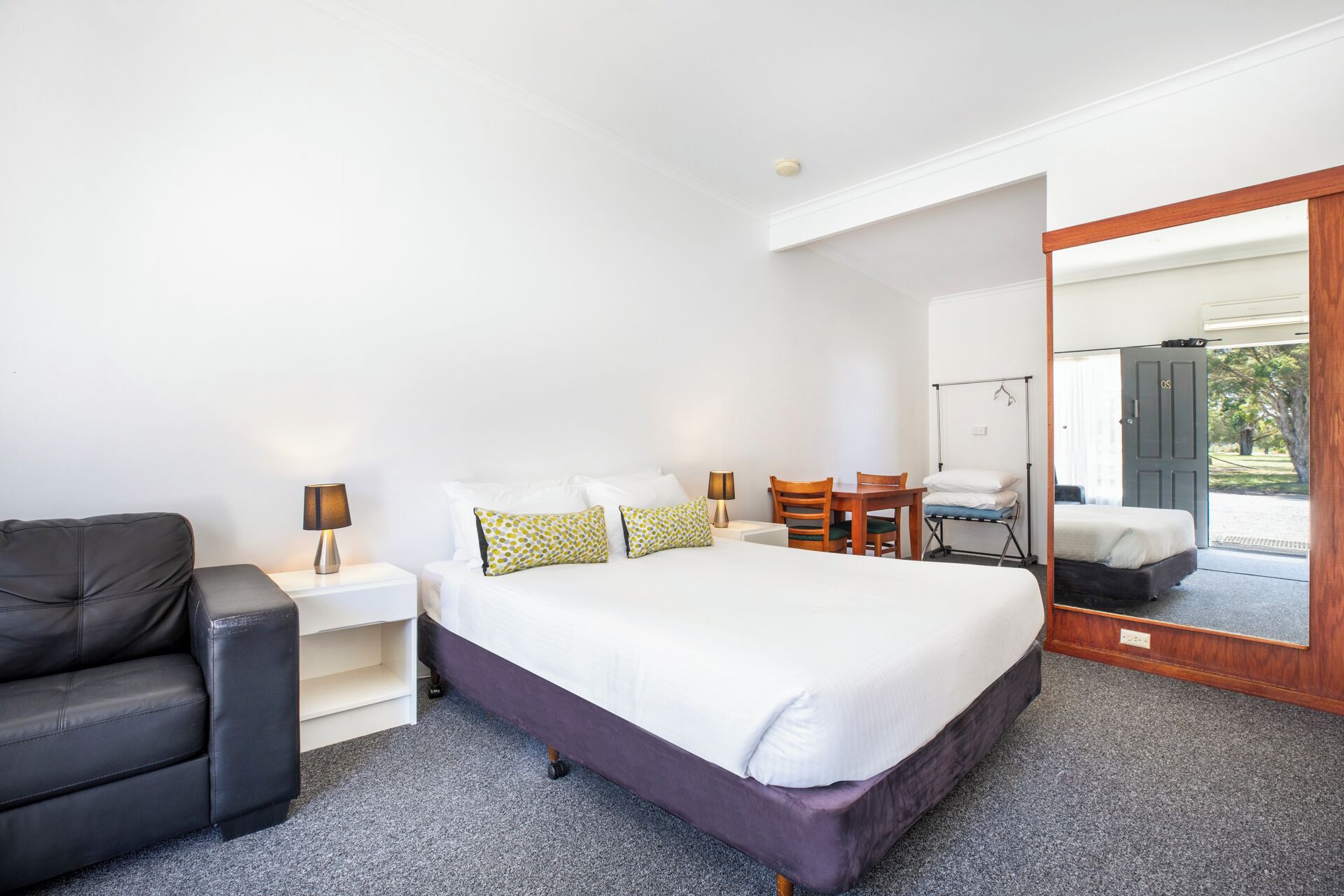 A bedroom with a large bed, a chair, a small table, and a mirror.