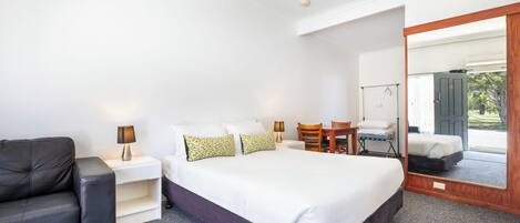 A bedroom with a large bed, a chair, a small table, and a mirror.