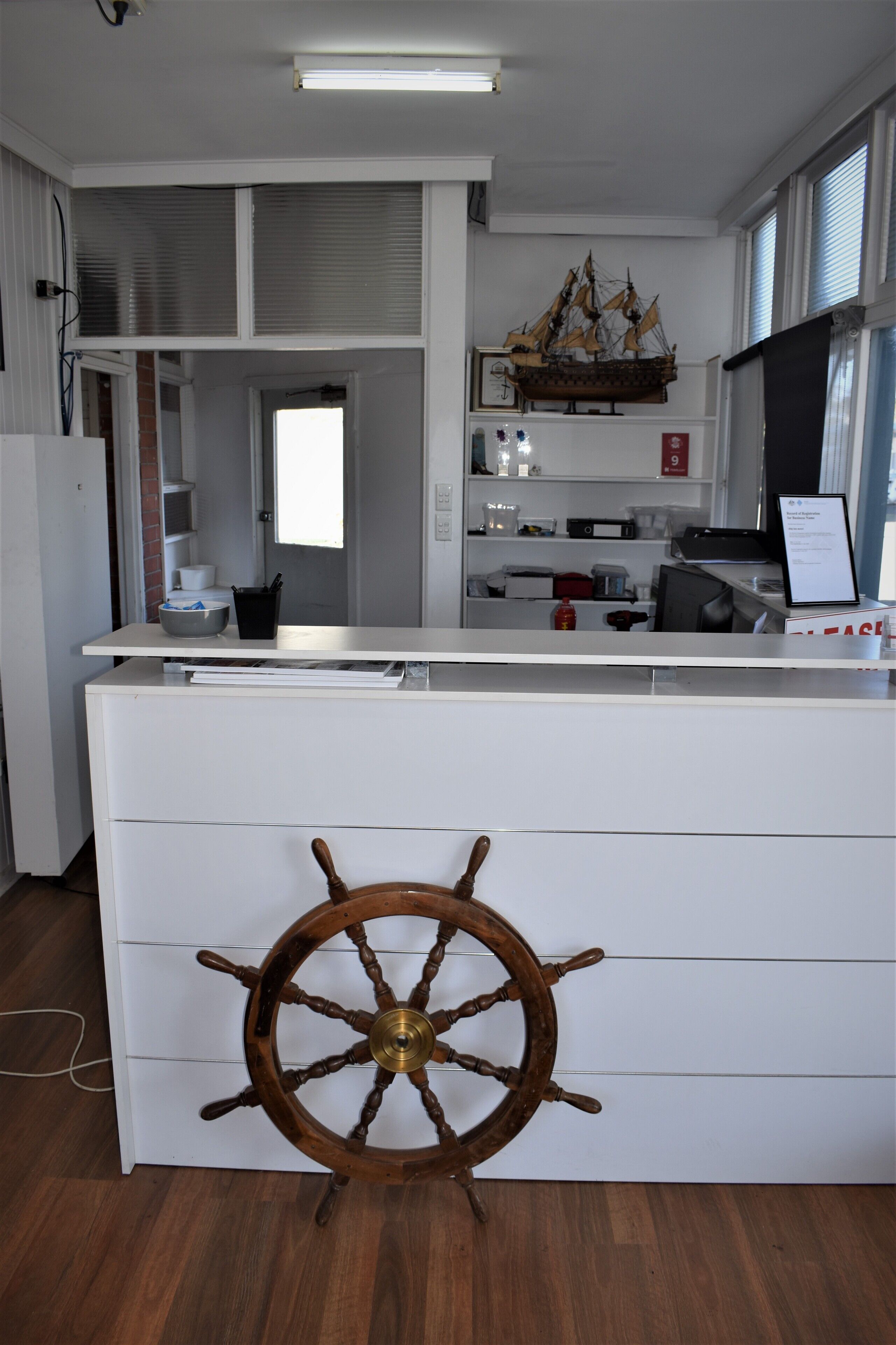 A kitchen with a wooden ship's wheel, white cabinetry, and a large window.