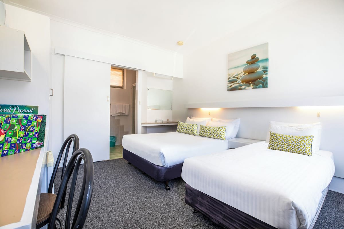 A hotel room with two beds, a desk, a chair, and a bathroom visible through an open door.