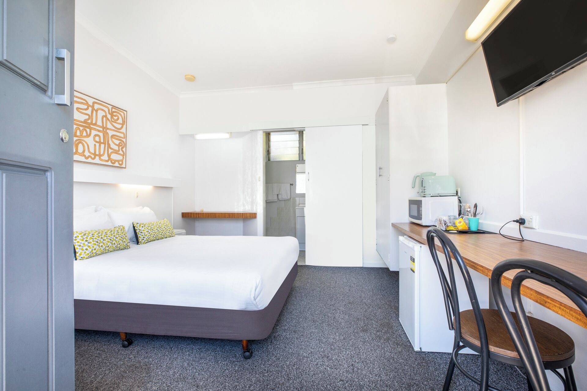 Een hotelkamer met een bed, een bureau, een stoel, een televisie en een kitchenette.