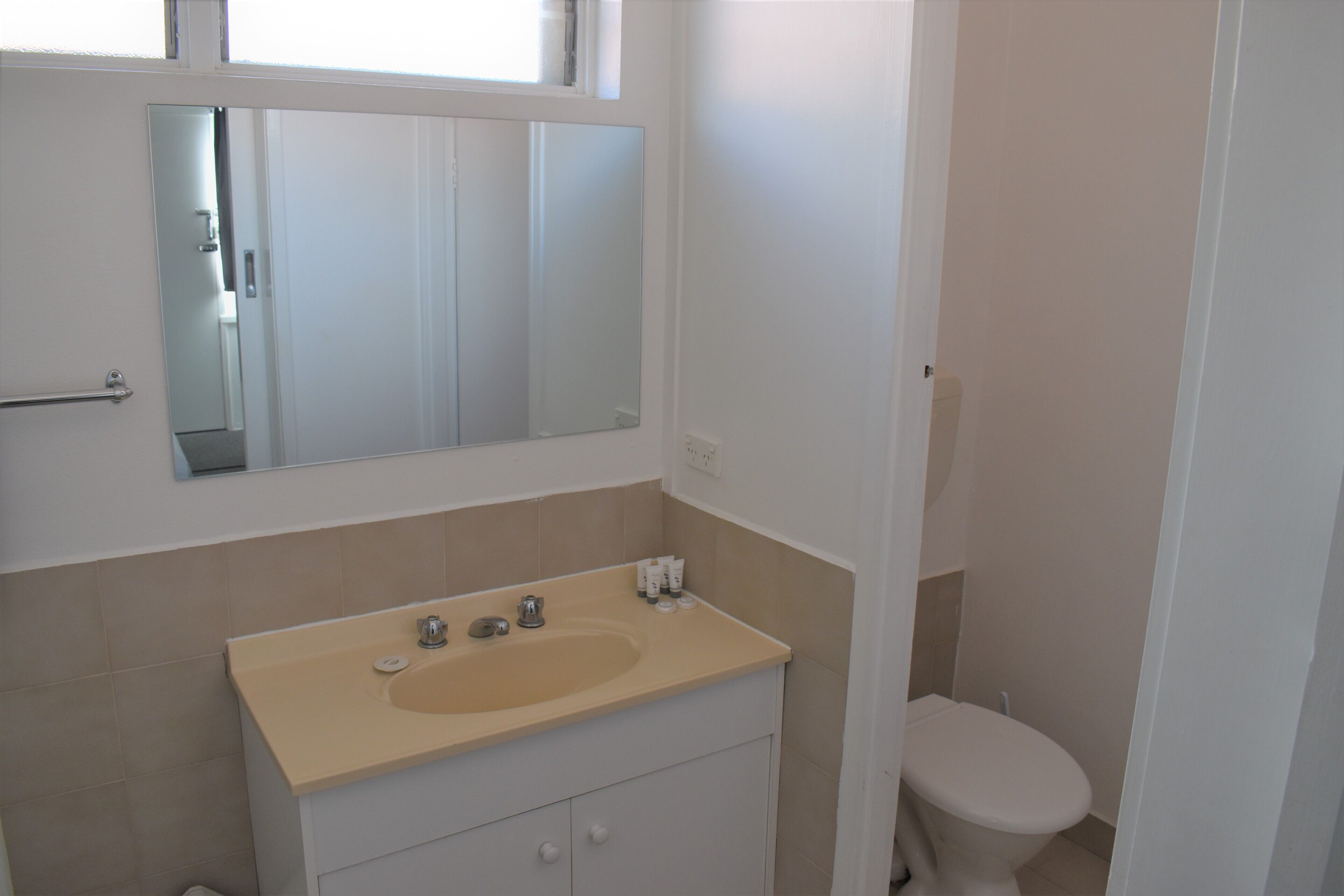 Une salle de bain avec un lavabo beige, un miroir au-dessus et des toilettes.