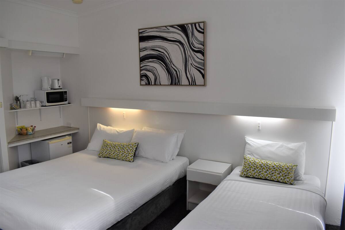 A hotel room with two beds, a microwave, a small refrigerator, and a shelf with toiletries.