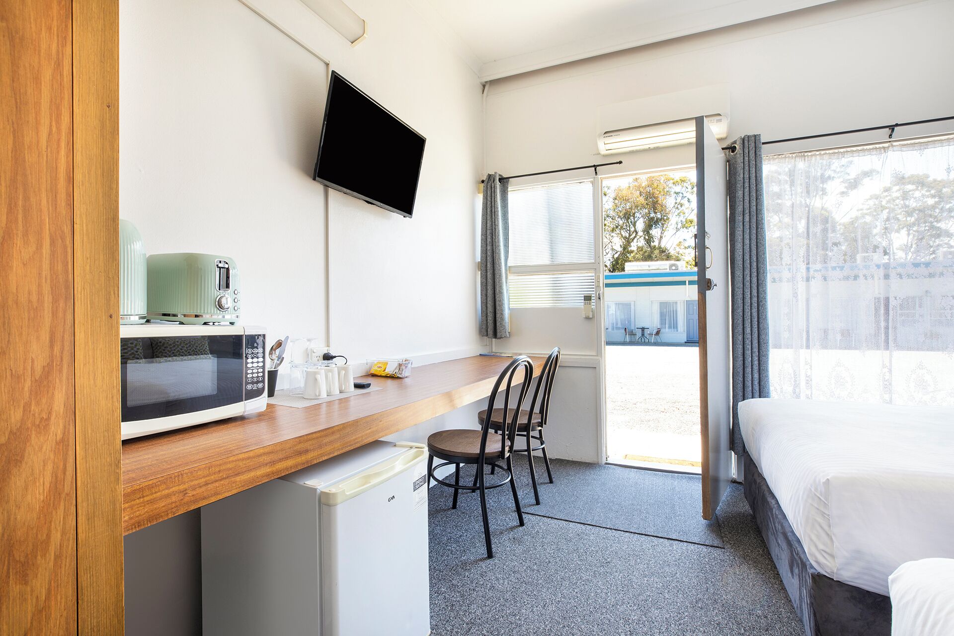A compact hotel room with a kitchenette, a bed, a desk, and a TV.