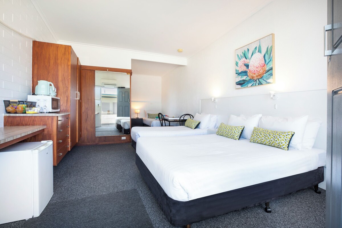 Een hotelkamer met een bed, een bureau met waterkoker, een stoel en een klein tafeltje.