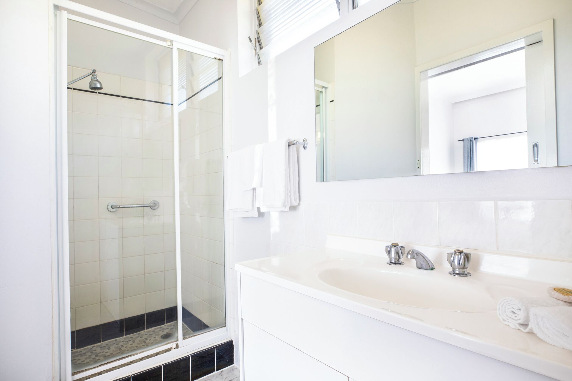 A modern bathroom with a glass shower enclosure, a white vanity with a sink, two faucets, and a large mirror.