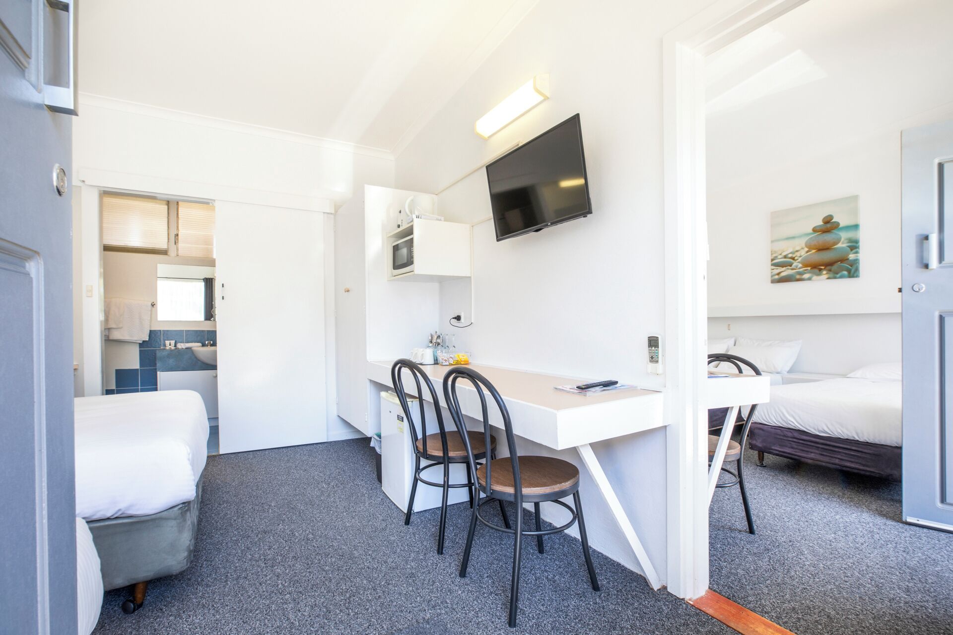 Une chambre d’hôtel compacte comprenant un coin cuisine, un lit, un bureau avec des chaises, une télévision et un tableau au mur.