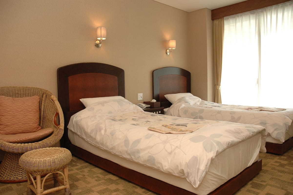 Une chambre d’hôtel avec deux lits, une chaise en osier et une table de chevet.