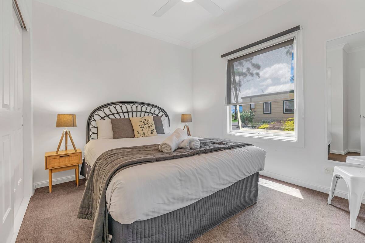 A bedroom with a bed, bedside lamps, a window, and a view of the outside.