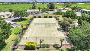 Ein Tennisplatz, umgeben von einem Zaun, mit Gebäuden und Bäumen im Hintergrund.