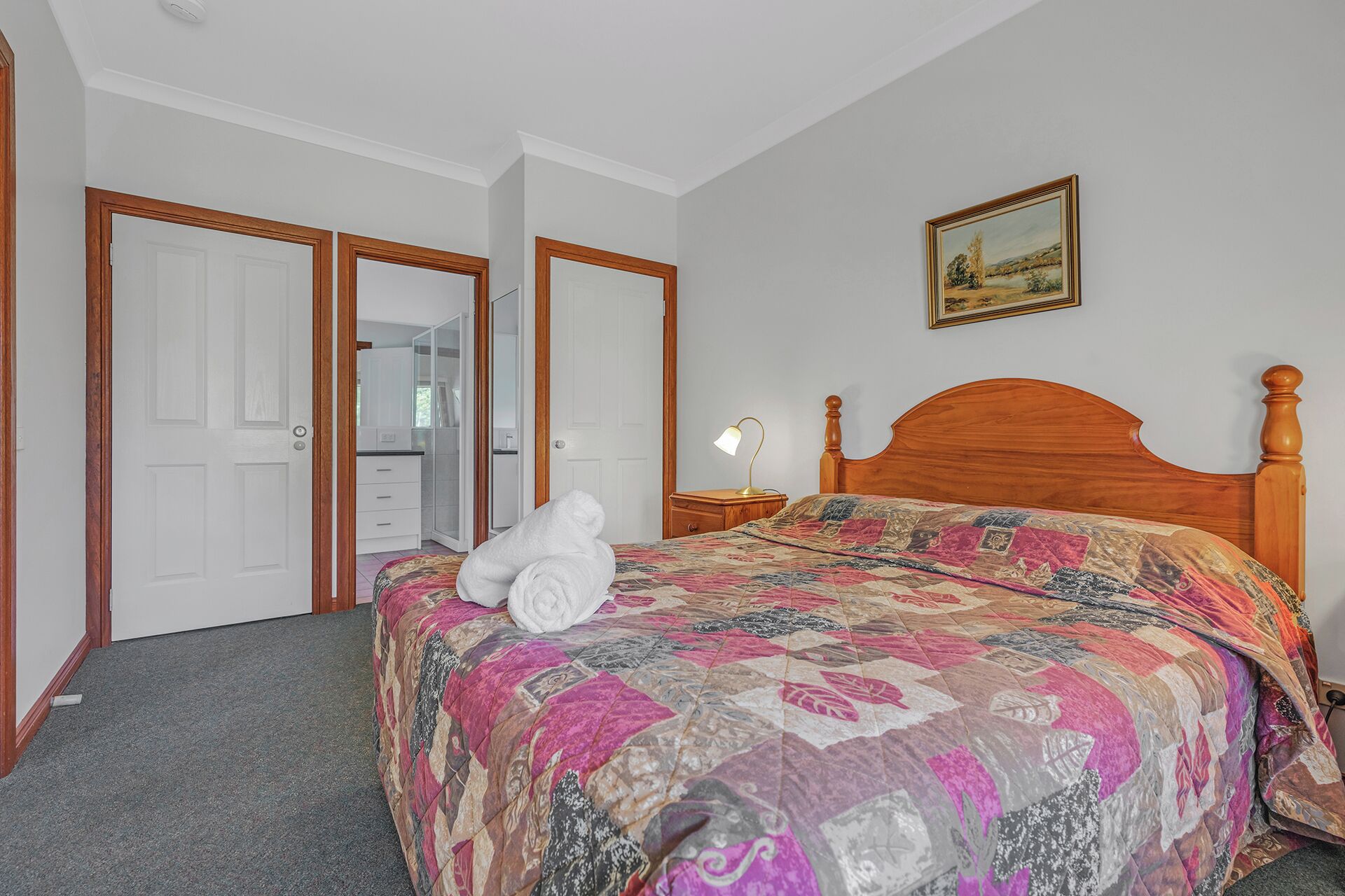 A bedroom with a wooden bed, a bedside lamp, and a painting on the wall.