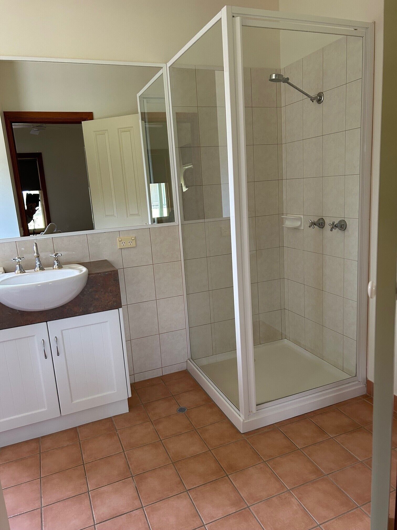 Baño con lavamanos blanco, espejo y cabina de ducha.