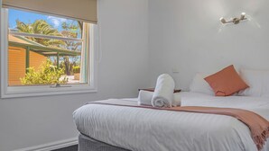 Ein Hotelzimmer mit einem Bett, einem Fenster mit Blick auf Palmen, einer Wandleuchte und einem kleinen Tisch mit einem Handtuch.