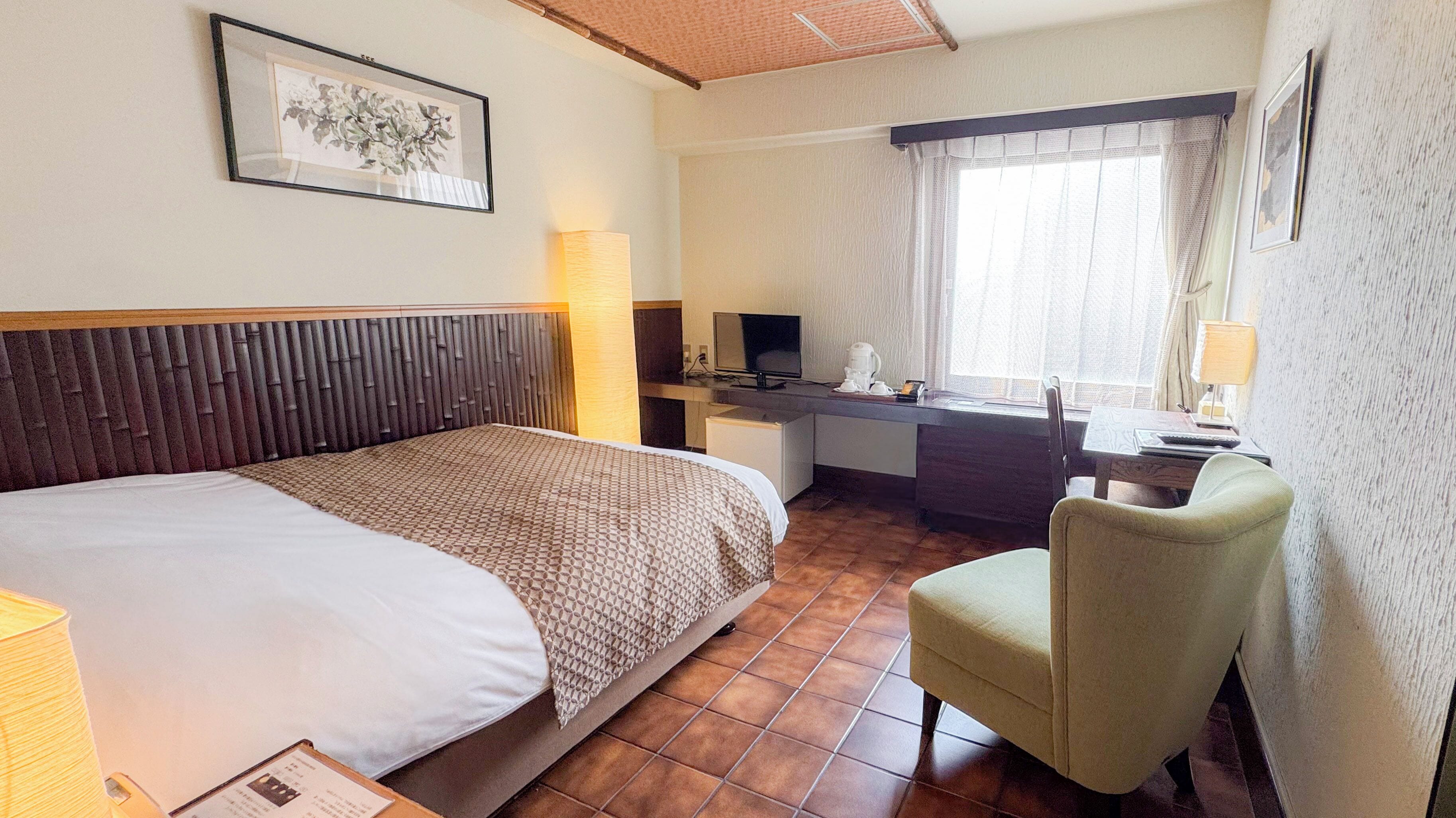 A hotel room with a large bed, a desk with a computer, a chair, and a window with curtains.