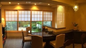 A room with a large sliding glass door leading to a garden, a dining table with chairs, and a chandelier.
