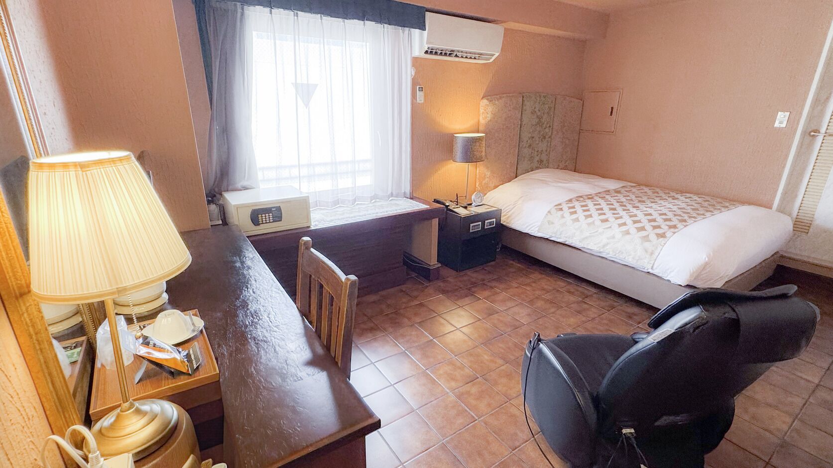 Ein Hotelzimmer mit Bett, Schreibtisch, Stuhl, Lampe und Klimaanlage.