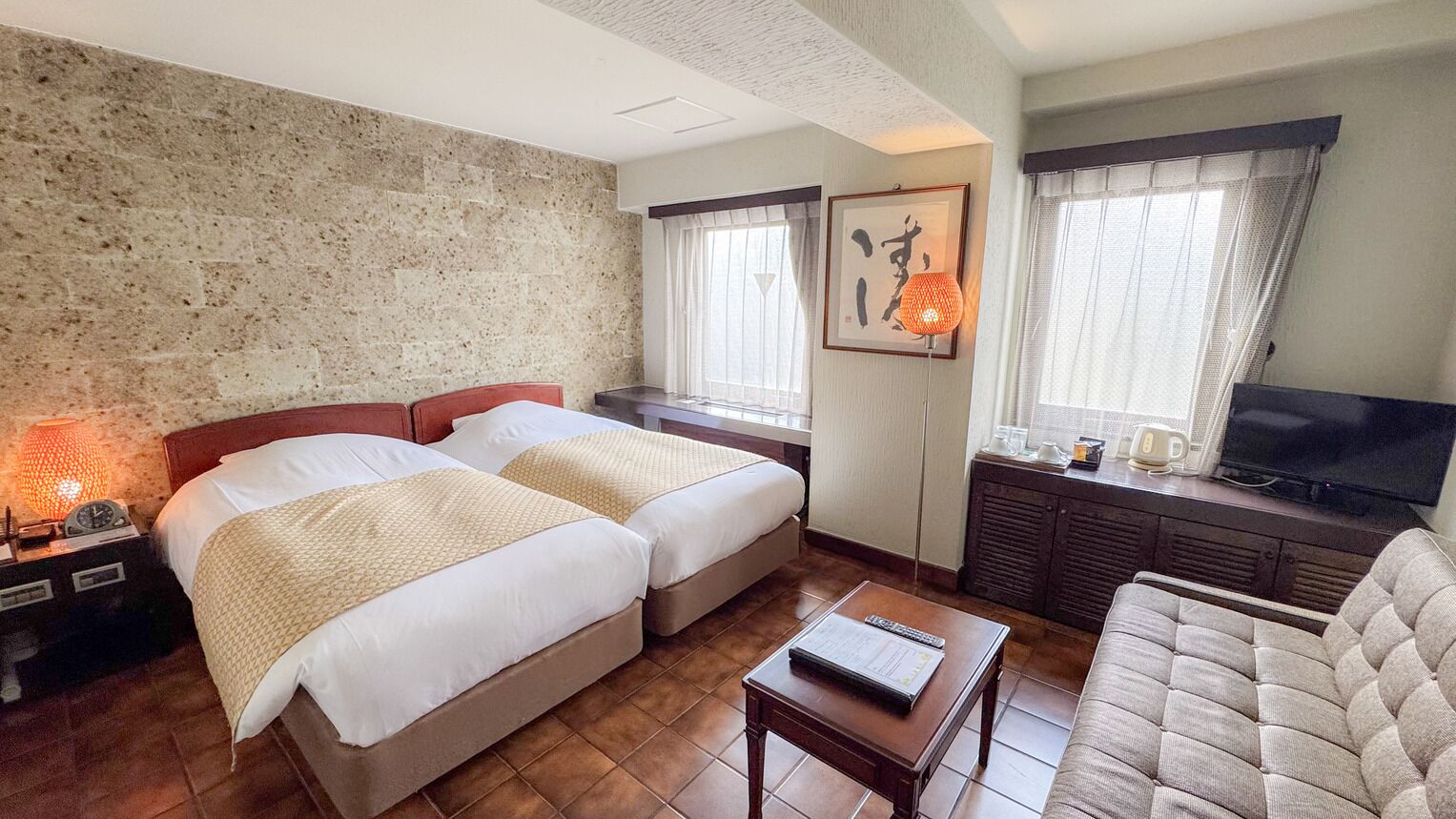 Ein Hotelzimmer mit zwei Betten, einem Sofa, einem Fernseher und einer Lampe.