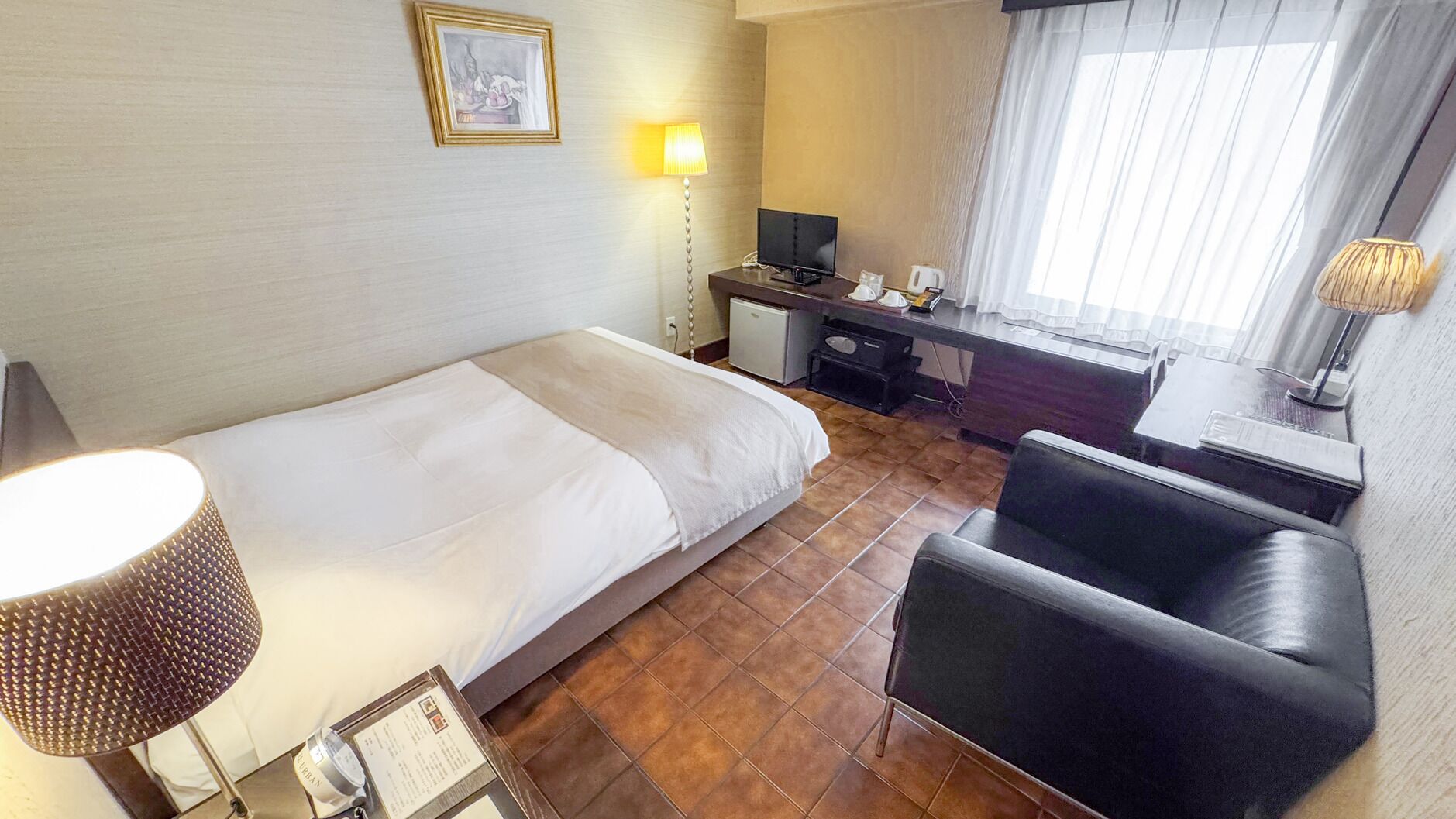 Ein Hotelzimmer mit Bett, Schreibtisch, Stuhl und einem kleinen Schrank.
