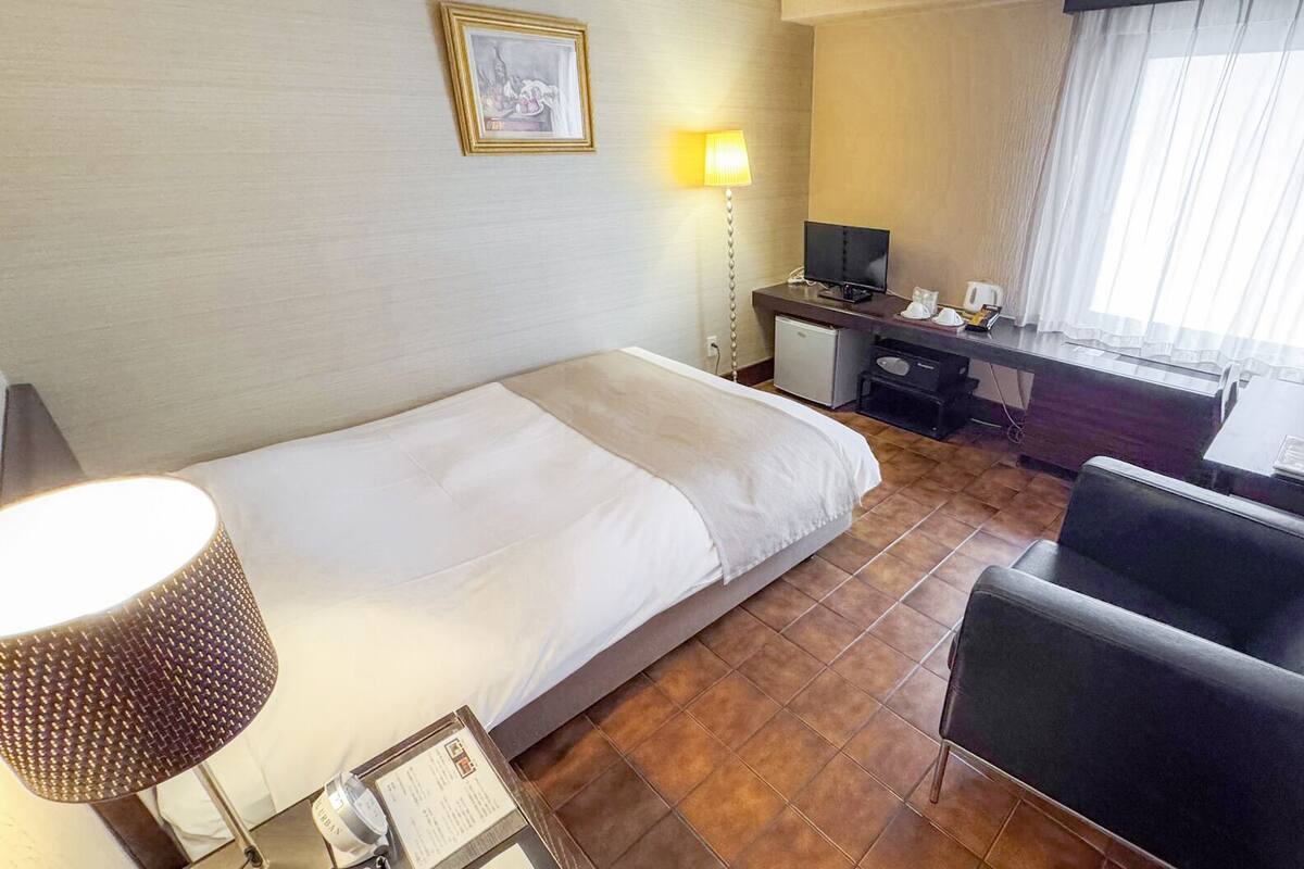 A hotel room with a bed, desk, chair, and a small cabinet.
