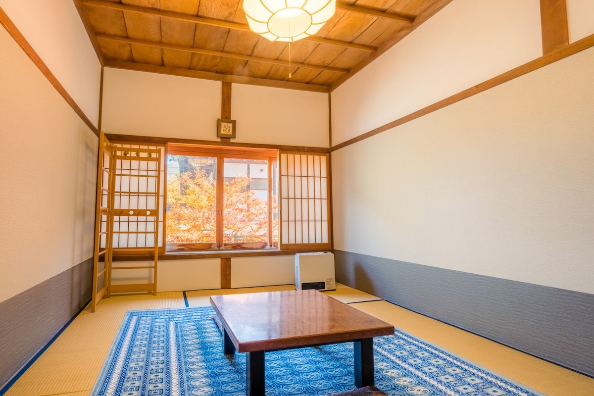 A traditional Japanese room with tatami flooring, a shoji screen, a wooden table, and a ceiling light fixture.