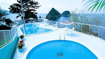 A pool area with a clear view of the sea, a lifeguard stand, and a seating area with umbrellas.