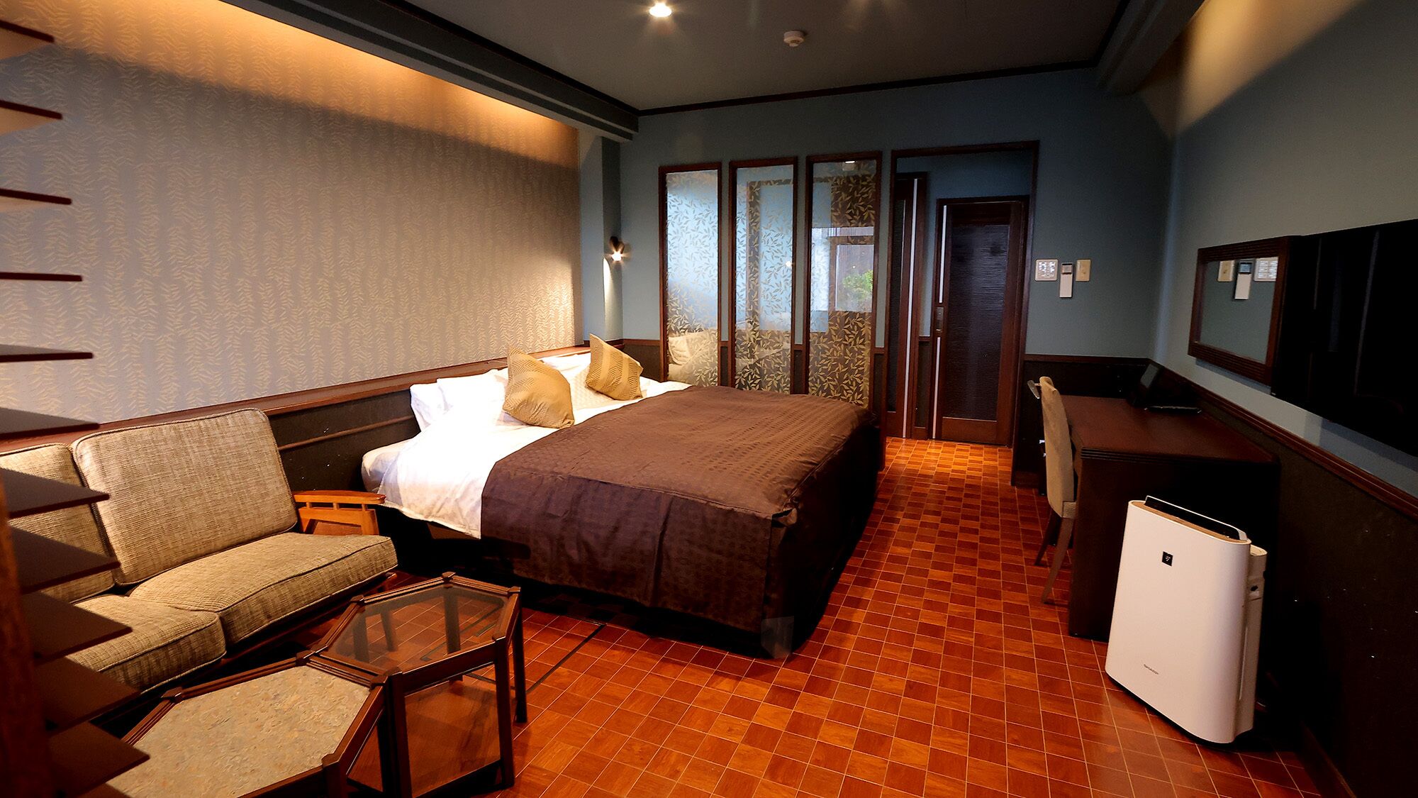 A hotel room with a bed, a sofa, a small table, a desk, and a refrigerator.
