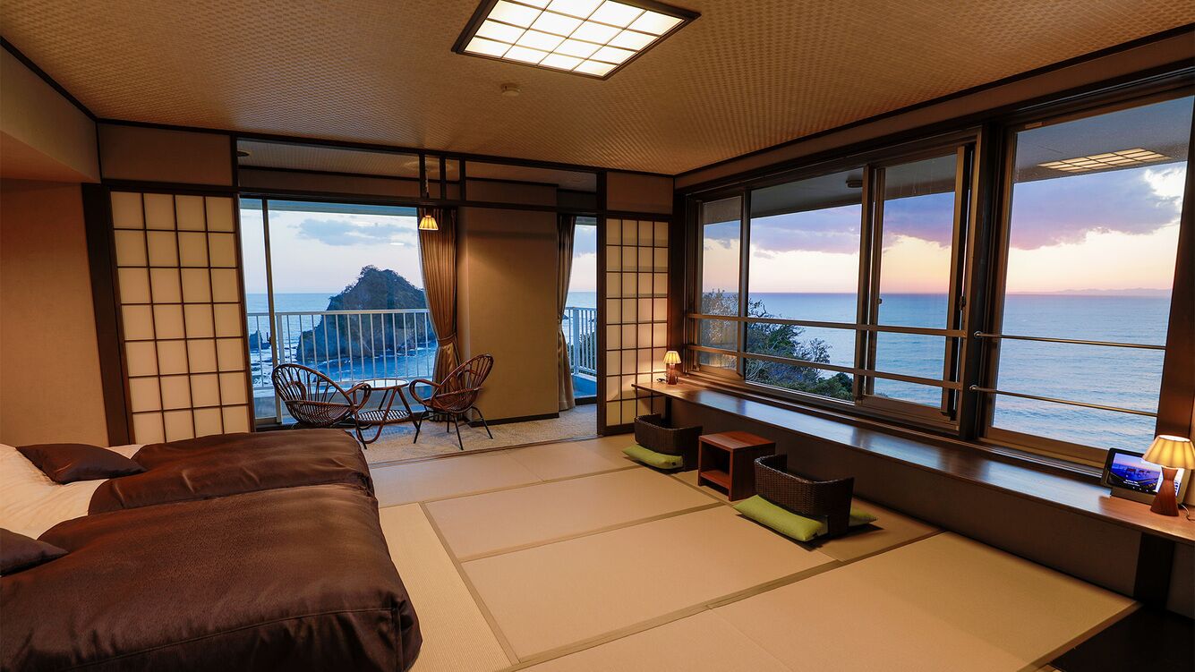 A room with tatami flooring, a bed, a seating area with cushions, and a view of the sea.