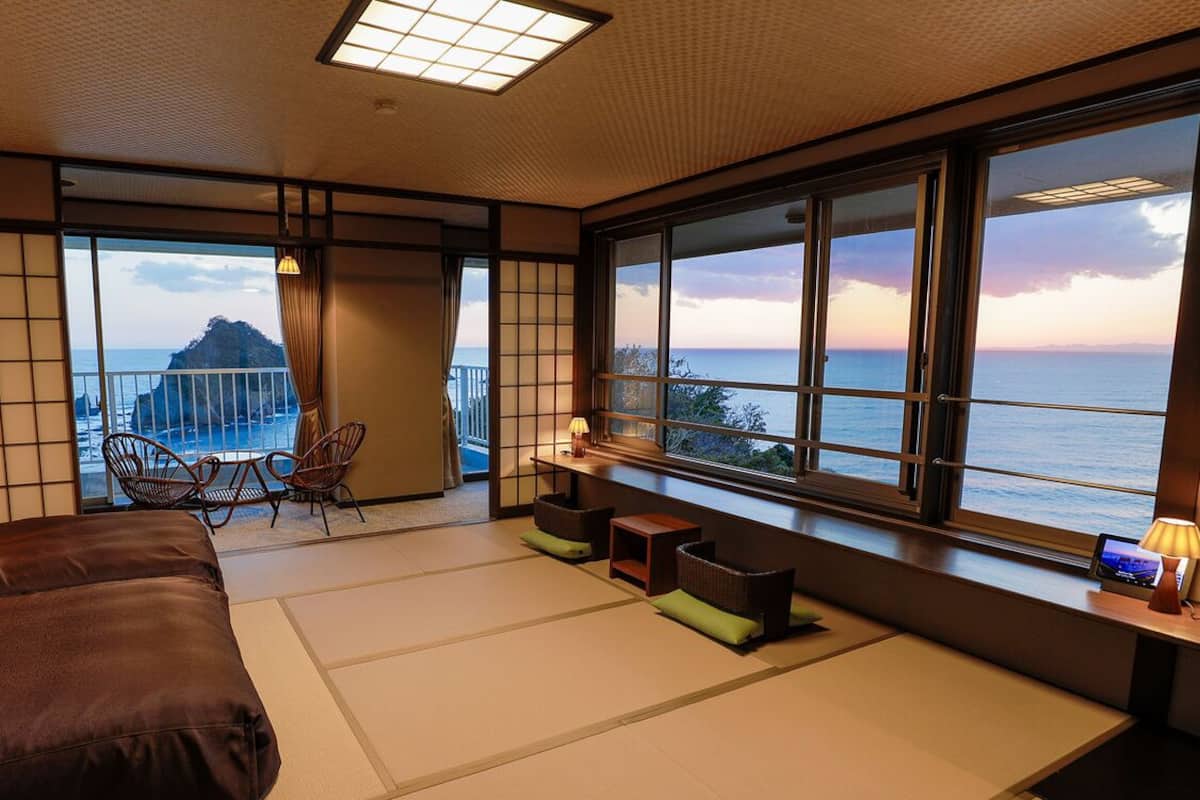 A room with tatami flooring, a bed, a seating area with cushions, and a view of the sea.