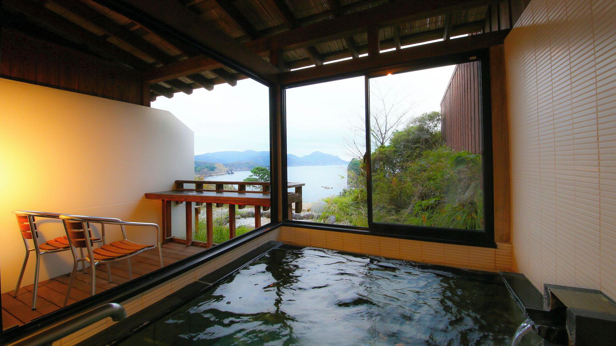 Een hottub met uitzicht op een meer en bergen, een houten tafel en een stoel.