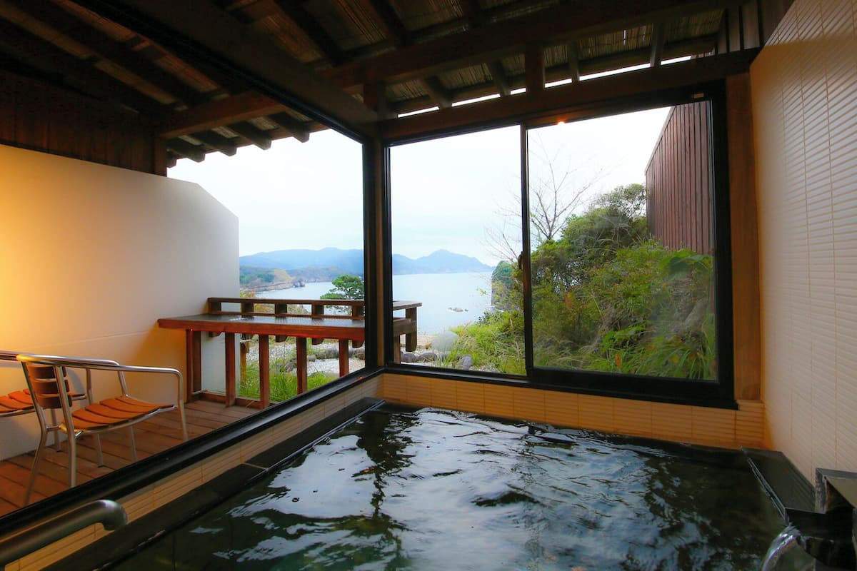 A hot tub with a view of a lake and mountains, a wooden table, and a chair.