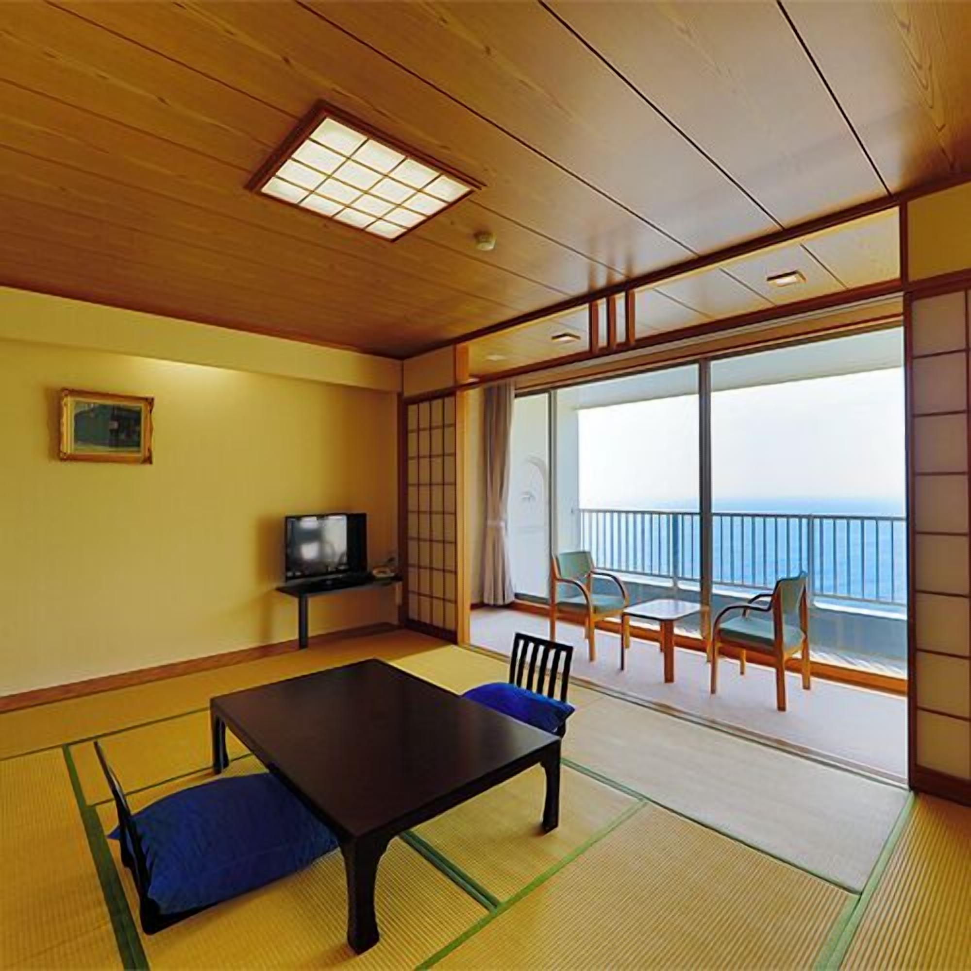 A room with tatami flooring, a low table, a television, and a balcony with a view.