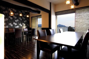 Un espace repas avec une grande table et des chaises, un mur décoré de motifs et une vue sur la mer.