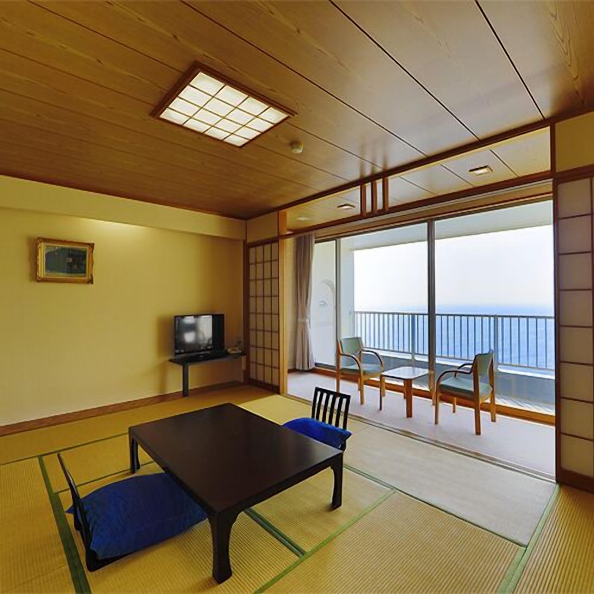 Een kamer met tatami matten, een lage tafel, stoelen, een televisietoestel en een groot raam met uitzicht.