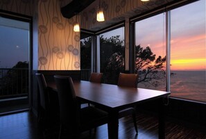 Un coin repas avec une table et des chaises, de grandes fenêtres offrant une vue sur le coucher de soleil et un papier peint à motifs.