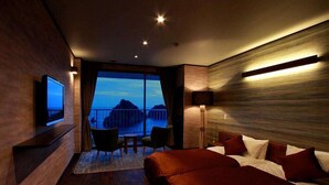 A modern hotel room with a large bed, a TV mounted on the wall, a balcony with a view of the sea, and a small seating area with a table and chairs. - Dogashima Hotel Tenyu (Nishiizu)