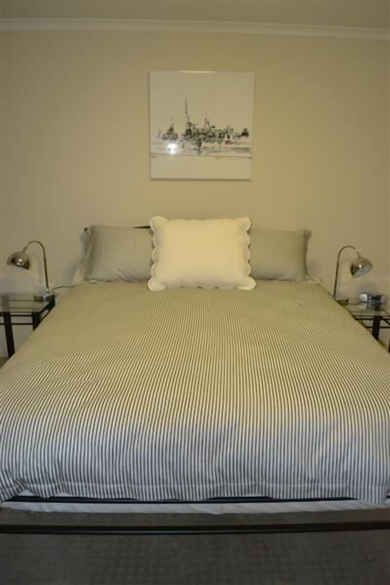 A neatly made bed with striped bedding, a single pillow, and two bedside lamps.